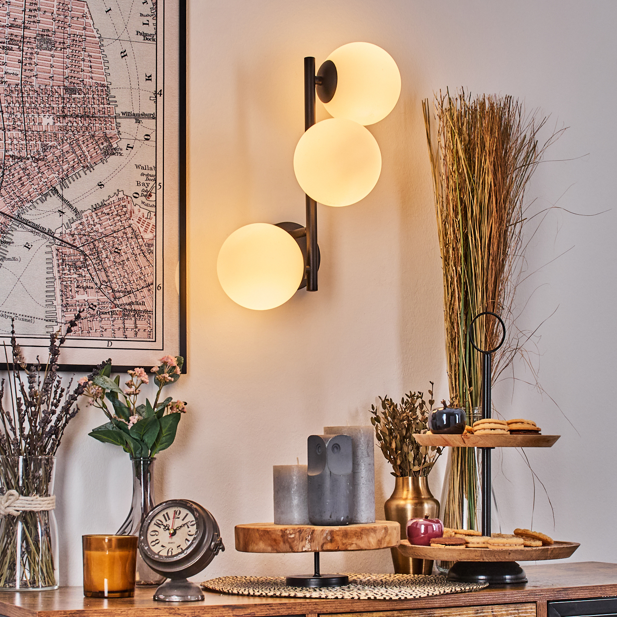 Ein Raum mit Wandlampe, Karte, Blumen, Uhr, Kerzen und Dekorationsartikeln auf einer Holzoberfläche.