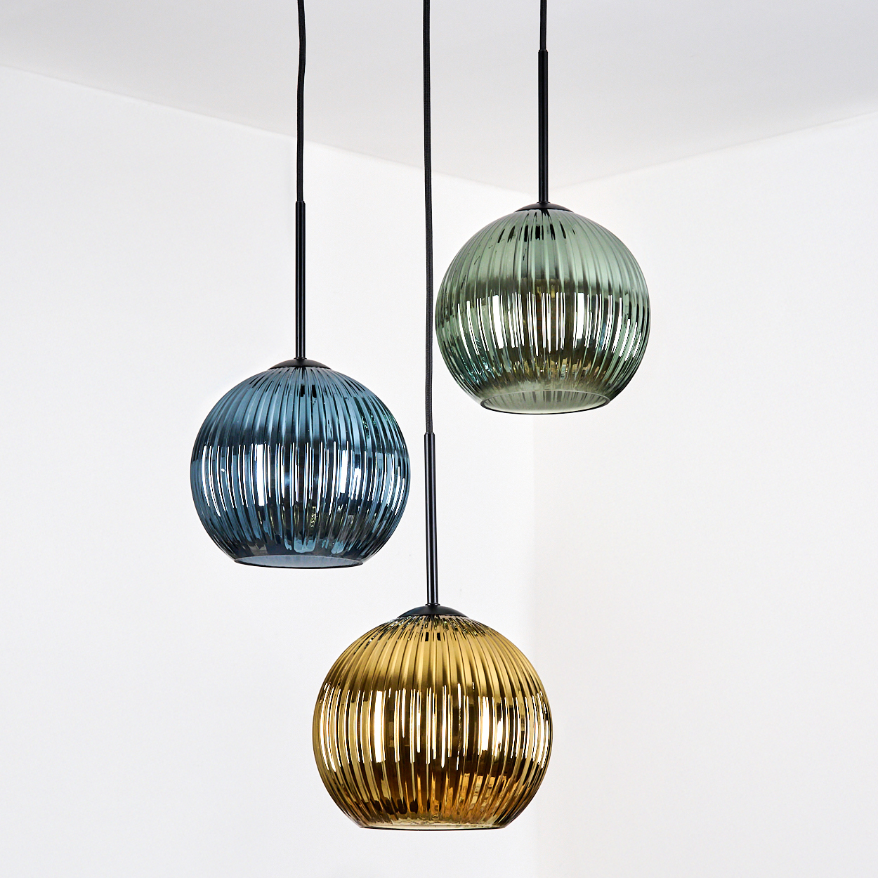 Drei kugelförmige Pendelleuchten in Blau, Grün und Gold hängen von der Decke in einer weißen Ecke.