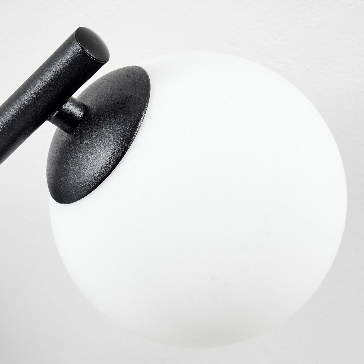 Nahaufnahme einer Lampe. Eine weiße Kugel wird teilweise von einer schwarzen Kappe und einem schwarzen Arm auf weißem Hintergrund bedeckt.