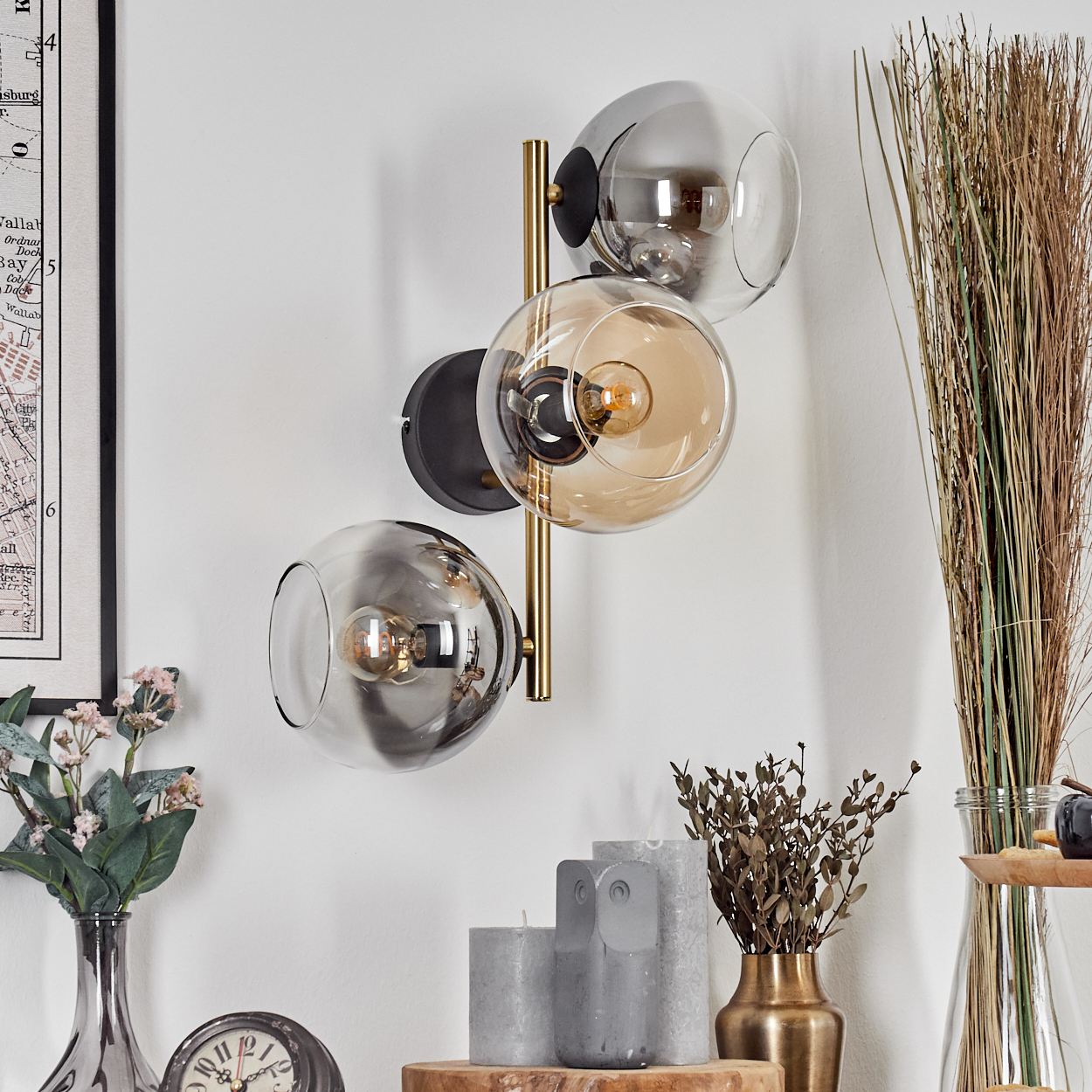 Eine moderne Wandlampe mit drei Glaskugeln. Darunter verschiedene Dekorationsartikel, darunter Kerzen und eine Vase.