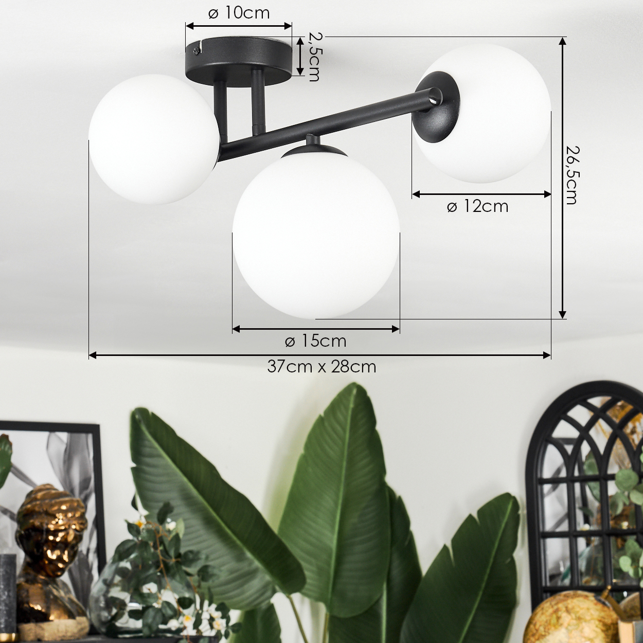 Eine moderne Deckenlampe mit drei weißen Kugeln und einem schwarzen Rahmen. Abmessungen sind angezeigt. Grüne Pflanzen befinden sich im Vordergrund.