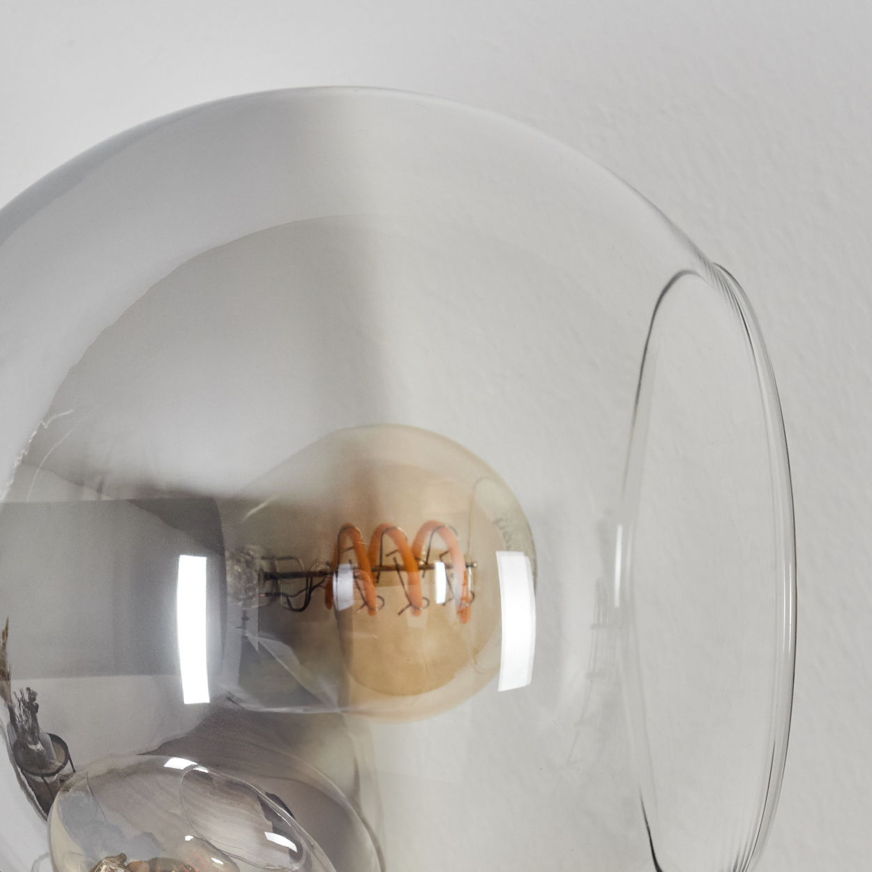Nahaufnahme einer Leuchte mit klarem Glasschirm. Im Inneren ist eine warmtonige Glühbirne mit Spiralfaden sichtbar.