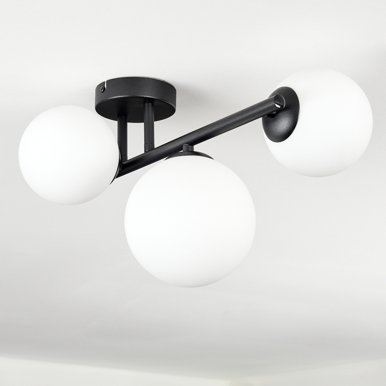 Moderne Deckenleuchte mit drei weißen Kugelschirmen und schwarzen Metallarmen, die an einer schwarzen Basis an der Decke befestigt sind.