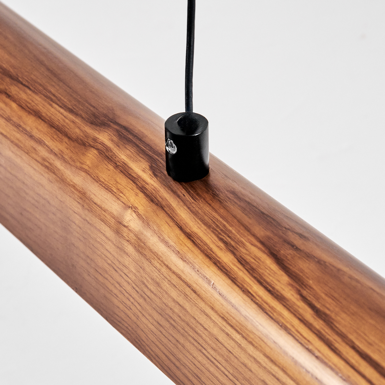 Nahaufnahme eines Holzbalkens mit einem schwarzen Zylinder und Draht, der von oben vor weißem Hintergrund hängt.