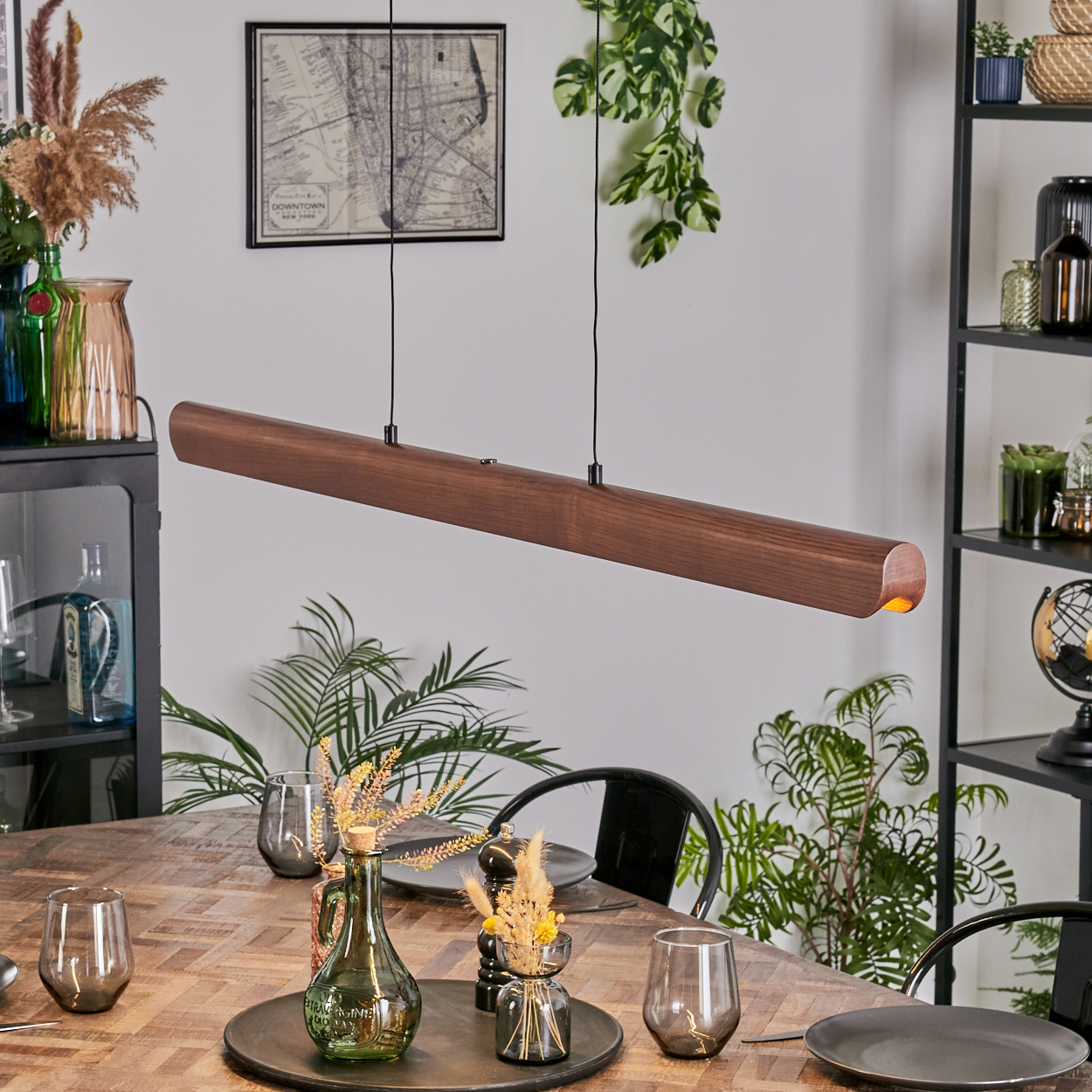 Ein modernes Esszimmer mit Holztisch, langer Holzleuchte und Pflanzen. Zubehör auf dem Tisch.