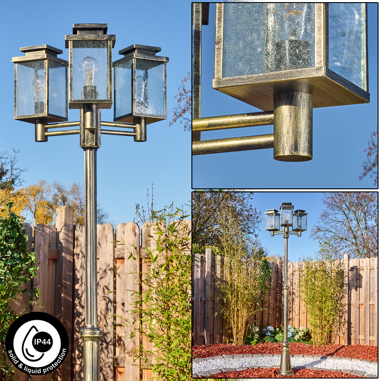 Eine Außenlaterne mit drei glaseingeschlossenen Lichtern. Die Stange ist goldfarben und vor einem Holzzaun und blauem Himmel angebracht.