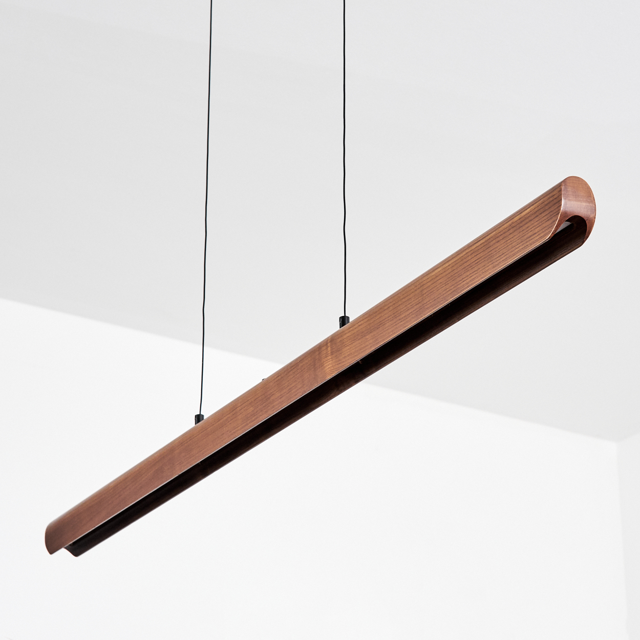 Eine moderne, lineare Holzleuchte hängt von der Decke. Sie ist braun und hat ein schlankes, minimalistisches Design mit schwarzen Kabeln.
