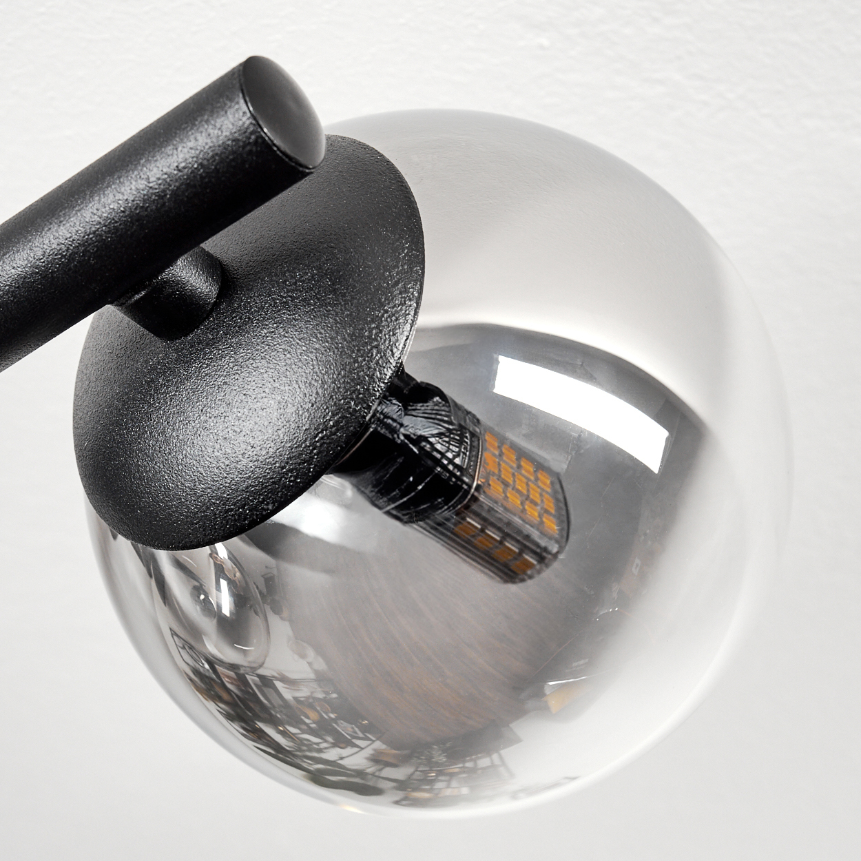 Nahaufnahme einer modernen Lampe. Sie hat einen schwarzen Metallarm und einen klaren, kugelförmigen Glasschirm mit einer orangefarbenen LED.