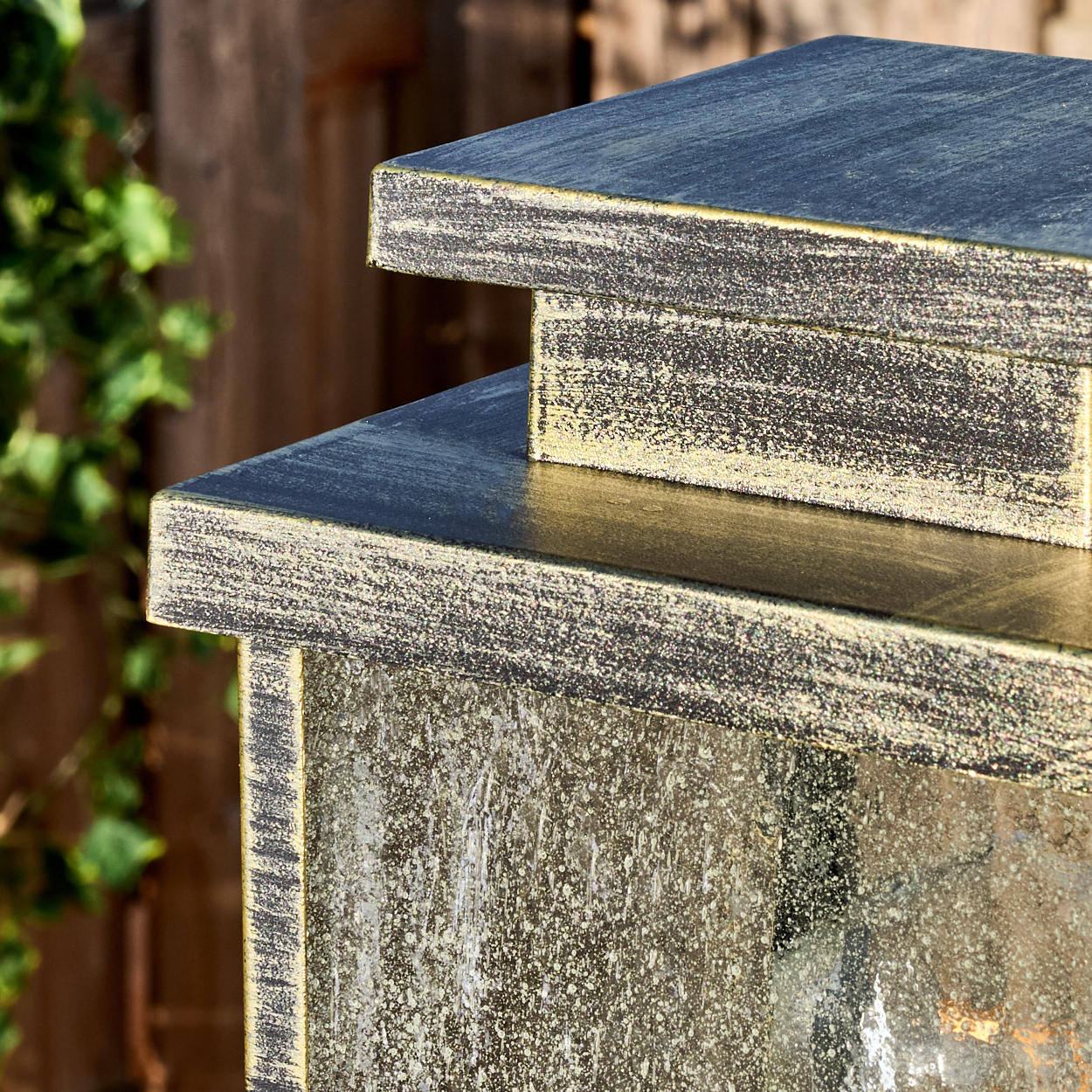 Nahaufnahme einer verwitterten, dunkelgrauen und goldfarbenen Metallstruktur mit mehrschichtigem Design, vor verschwommenem Holz.