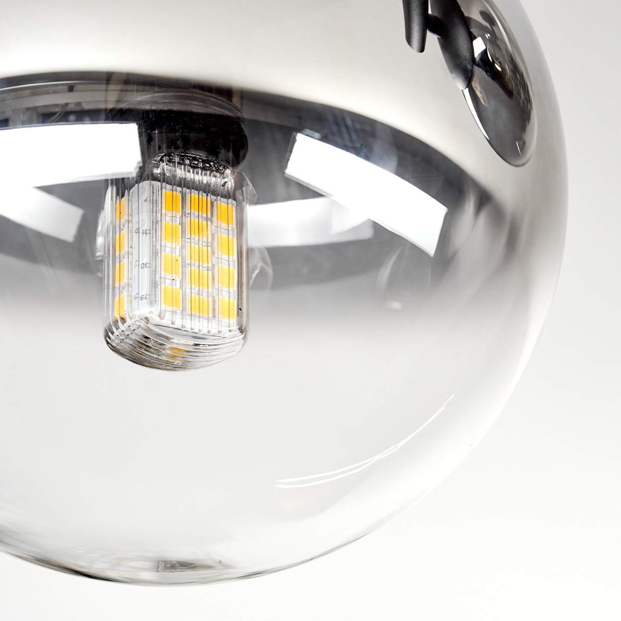 Nahaufnahme einer klaren Glaskugelleuchte. Im Inneren leuchtet eine rechteckige LED-Lampe. Der Hintergrund ist weiß.