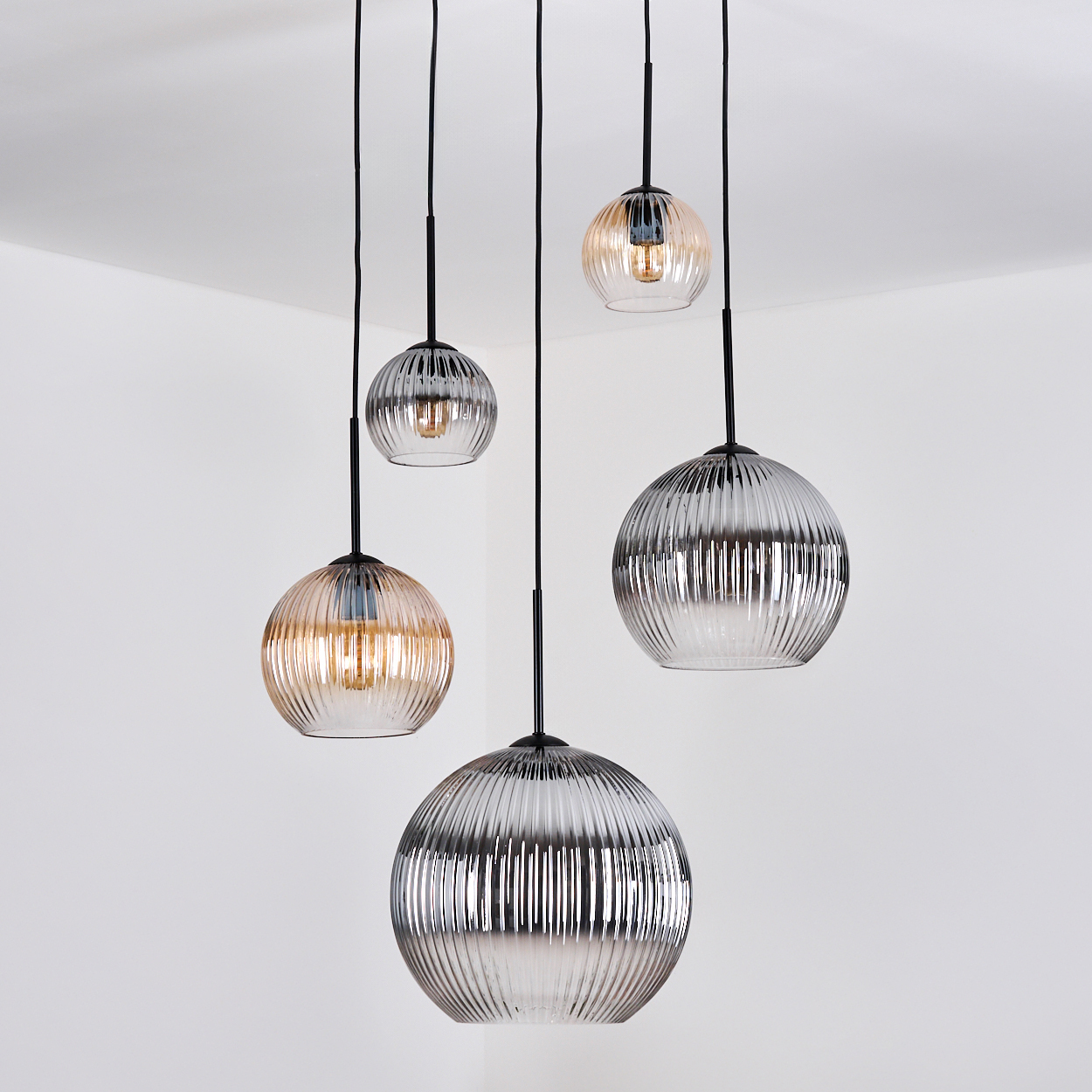 Fünf Glas-Kugel-Pendelleuchten hängen von der Decke. Die Kugeln haben verschiedene Farben und Größen vor einem weißen Hintergrund.