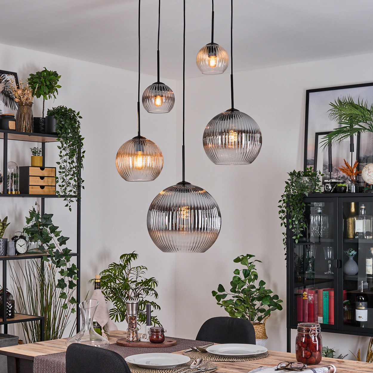 Esszimmer mit Hängelampen, einem Holztisch, Pflanzen und einem schwarzen Schrank. Die Lampen haben eine kugelförmige Form.