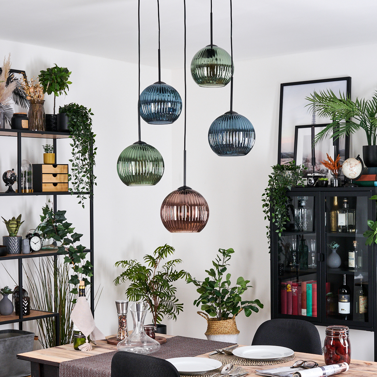 Esszimmer mit Holztisch, Zierpflanzen, hängenden Glaslampen und einem schwarzen Schrank.