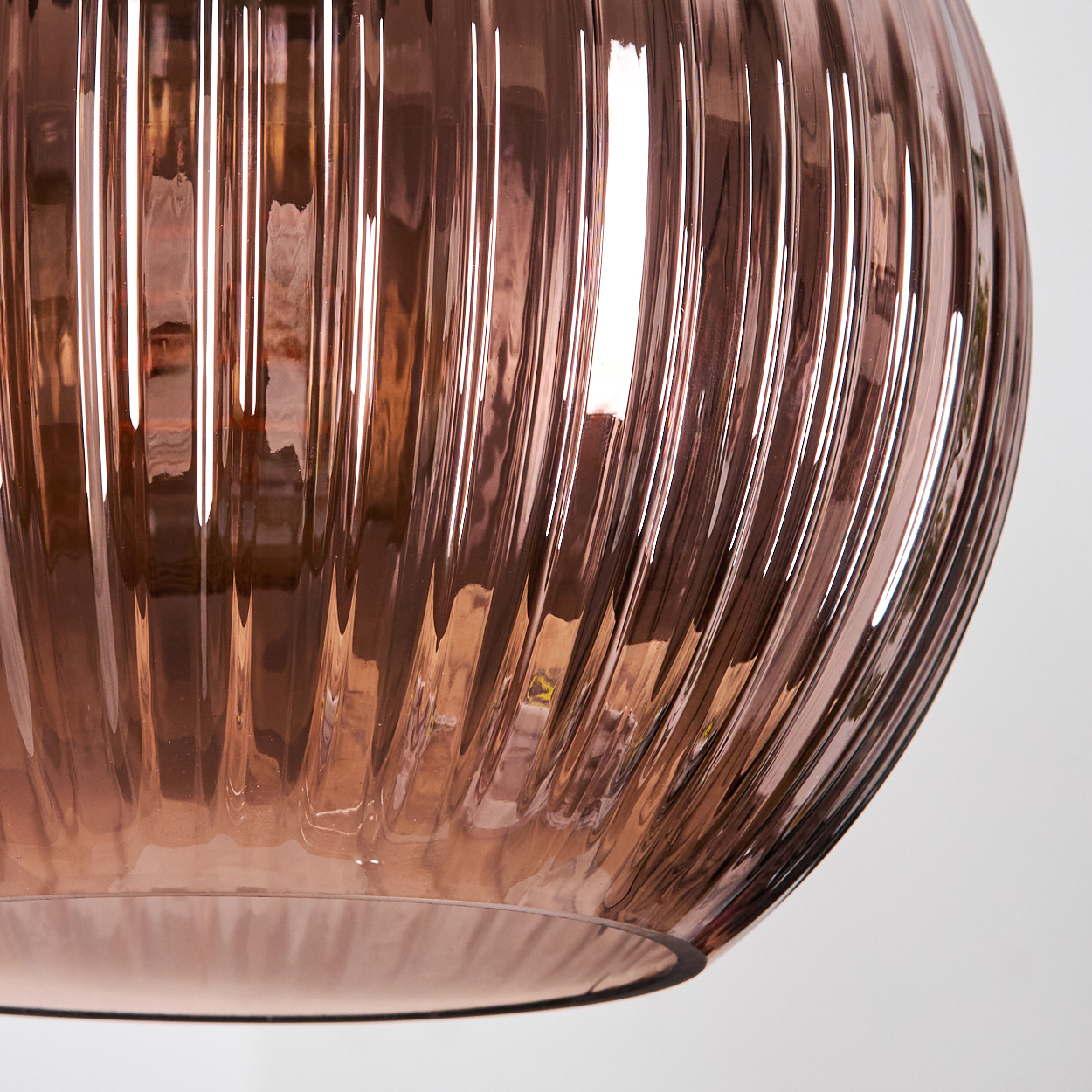 Nahaufnahme eines roségoldenen Glasobjekts mit vertikalen Rippen. Das Licht reflektiert auf der Glasoberfläche und erzeugt Glanzlichter und Schatten.