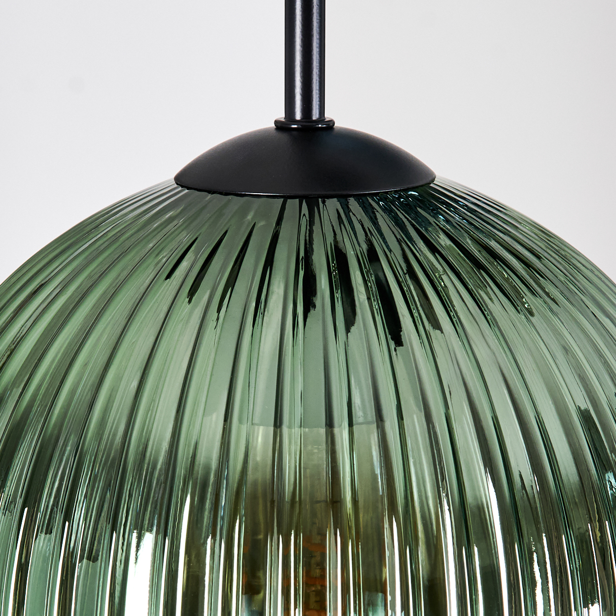 Nahaufnahme einer grünen, gerippten Glas-Pendelleuchte mit schwarzem Metallaufsatz und -stiel, vor weißem Hintergrund.