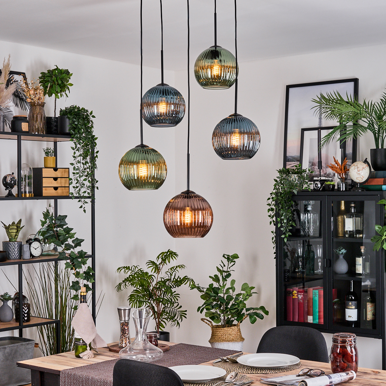 Esszimmer mit Hängeleuchten, Pflanzen, Tisch gedeckt. Schwarze Regale und Schrank mit Dekoration.