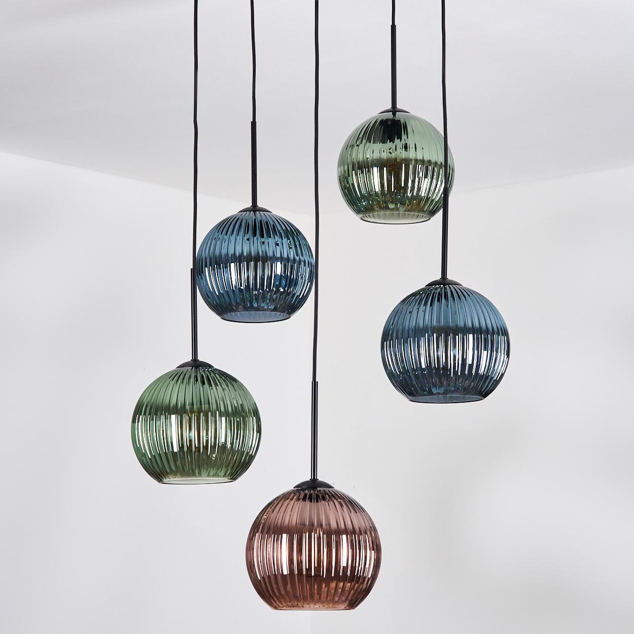 Fünf Pendelleuchten aus Glas in Grün-, Blau- und Rosatönen hängen von einer weißen Decke.
