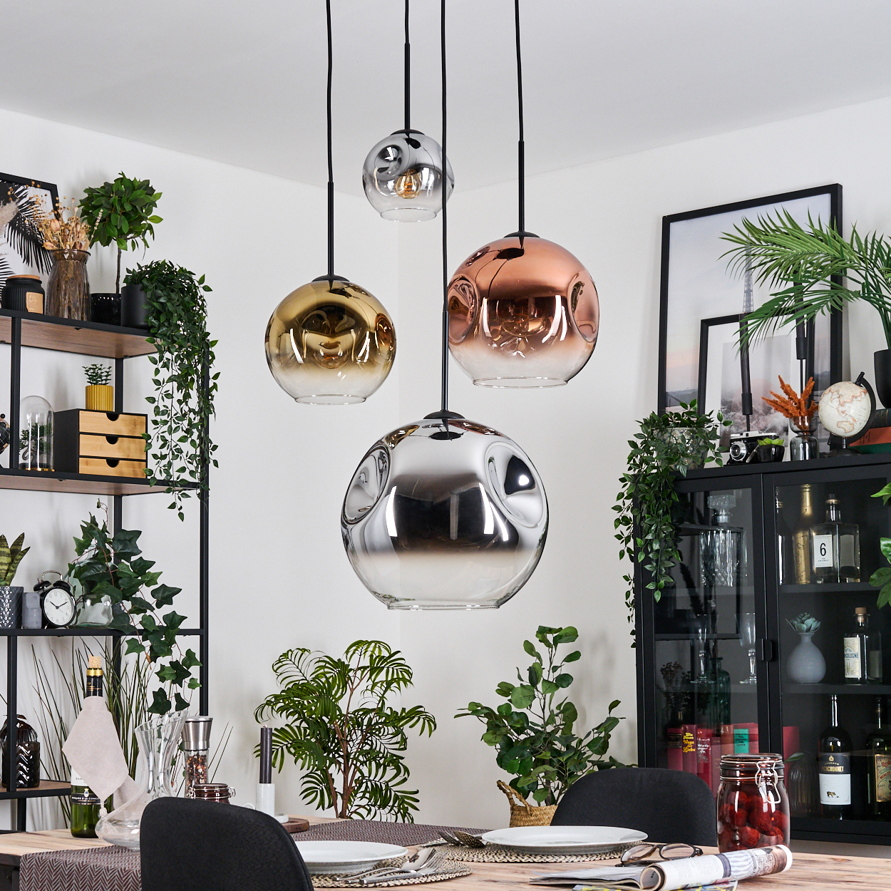 Esszimmer mit Hängeleuchten. Goldene, kupferfarbene und silberne Kugeln. Pflanzen, Regale und ein gedeckter Tisch.