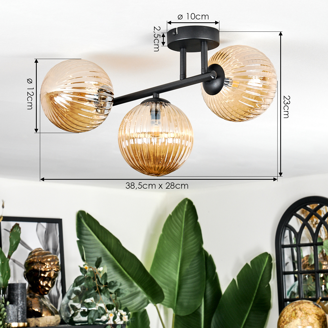 Eine moderne Deckenlampe mit drei bernsteinfarbenen Glaskugeln. Sie befindet sich über einer Pflanze und einer dekorativen Büste.