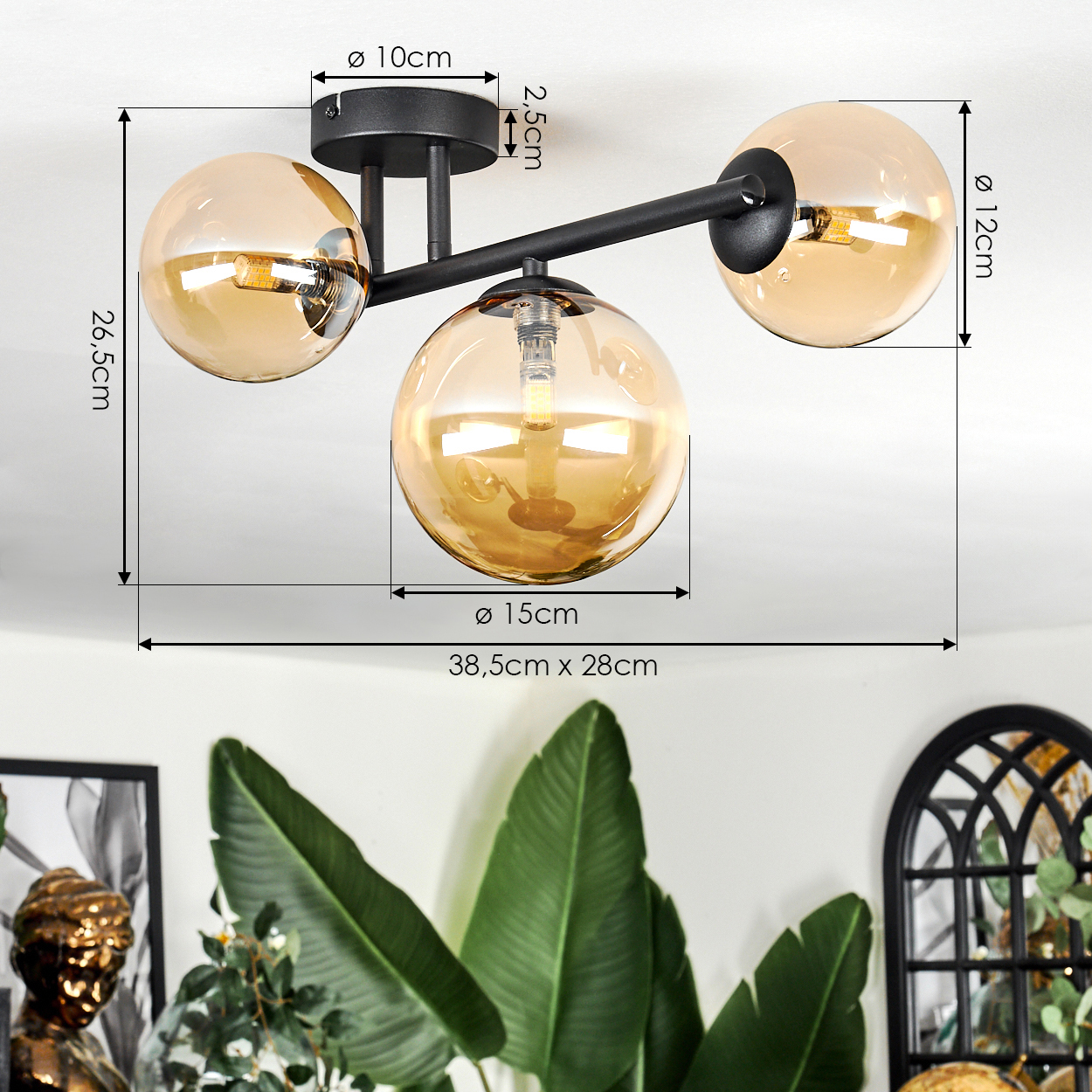 Eine moderne Deckenlampe mit drei bernsteinfarbenen Glaskugeln, schwarzen Halterungen und grünen Blättern im Hintergrund.