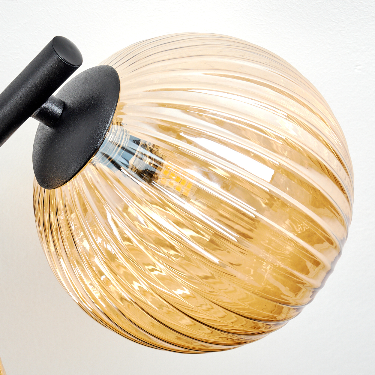Nahaufnahme einer Lampe mit einem kugelförmigen, bernsteinfarbenen Glasschirm. Der Schirm hat ein Rippenmuster und ein schwarzer Arm und eine Halterung stützen ihn.