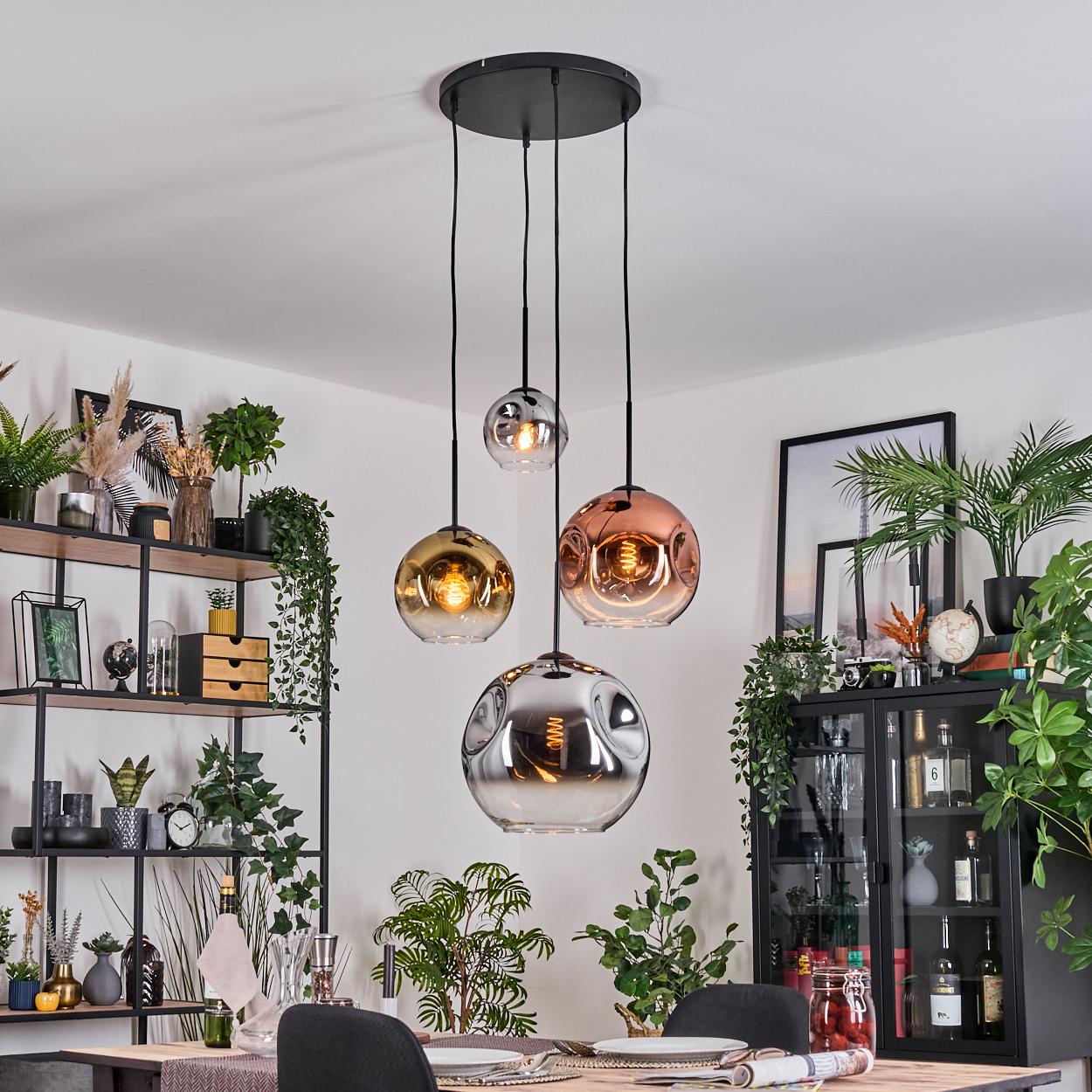 Drei Pendelleuchten mit Glaskugeln hängen über einem Tisch. Links ein Regal mit Pflanzen und Deko. Rechts ein Schrank.
