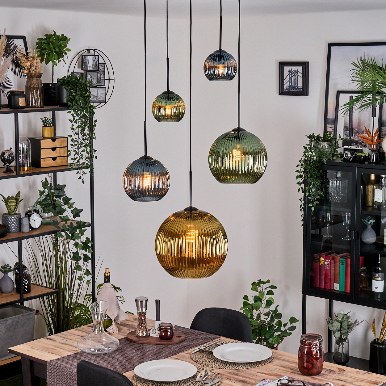 Esszimmer mit hängenden Glaslampen. Tisch für das Abendessen gedeckt. Regale mit Pflanzen und Dekoration. Schwarzer Schrank mit Büchern.