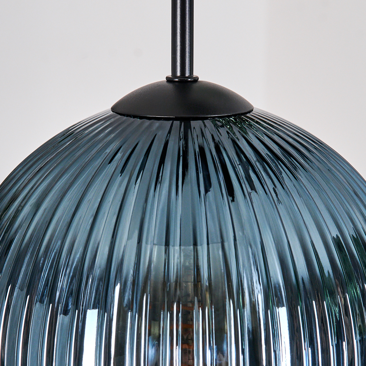 Nahaufnahme einer blauen Glas-Hängeleuchte. Der Schirm ist gerippt und kuppelförmig, mit schwarzer Metallbefestigung.