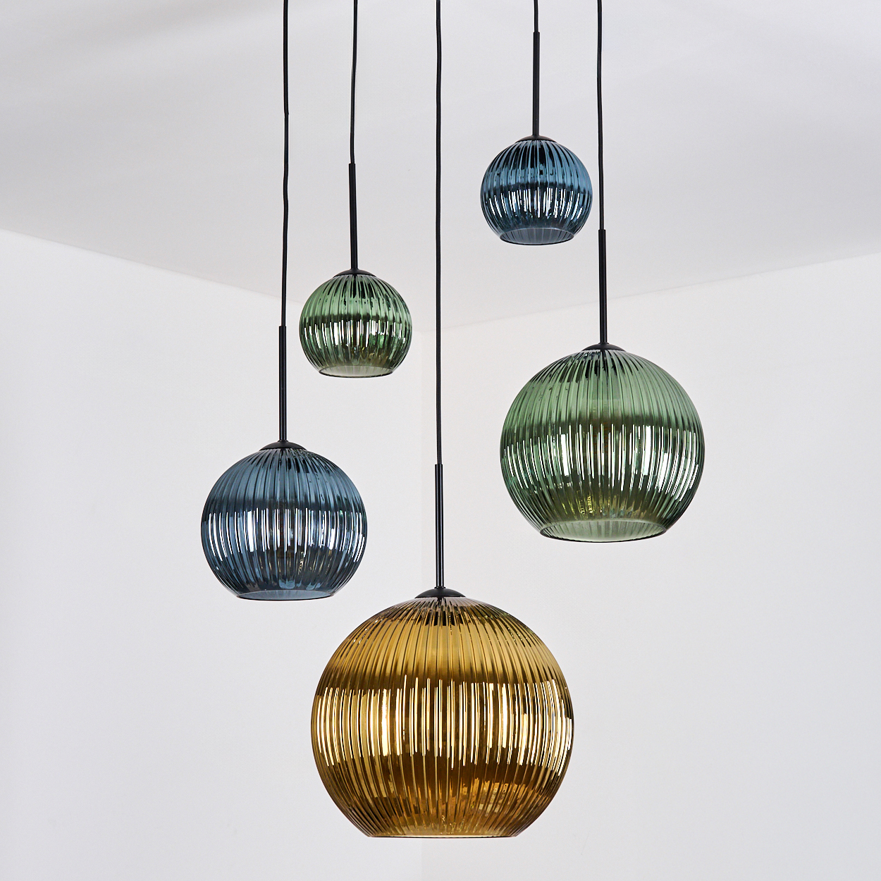 Fünf Glas-Pendelleuchten in verschiedenen Farben hängen von der Decke. Sie haben eine gerippte Textur und schwarze Kabel.