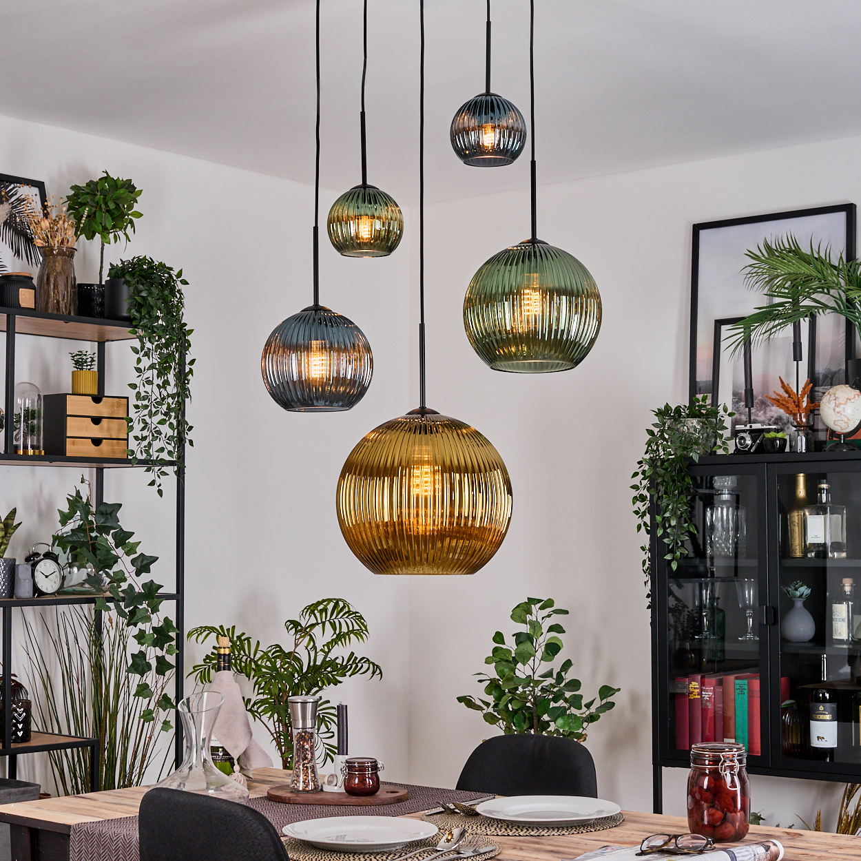 Esszimmer mit hängenden Kugelleuchten in verschiedenen Farben. Tisch gedeckt. Regale und Schrank mit Dekor und Pflanzen vervollständigen die Szene.