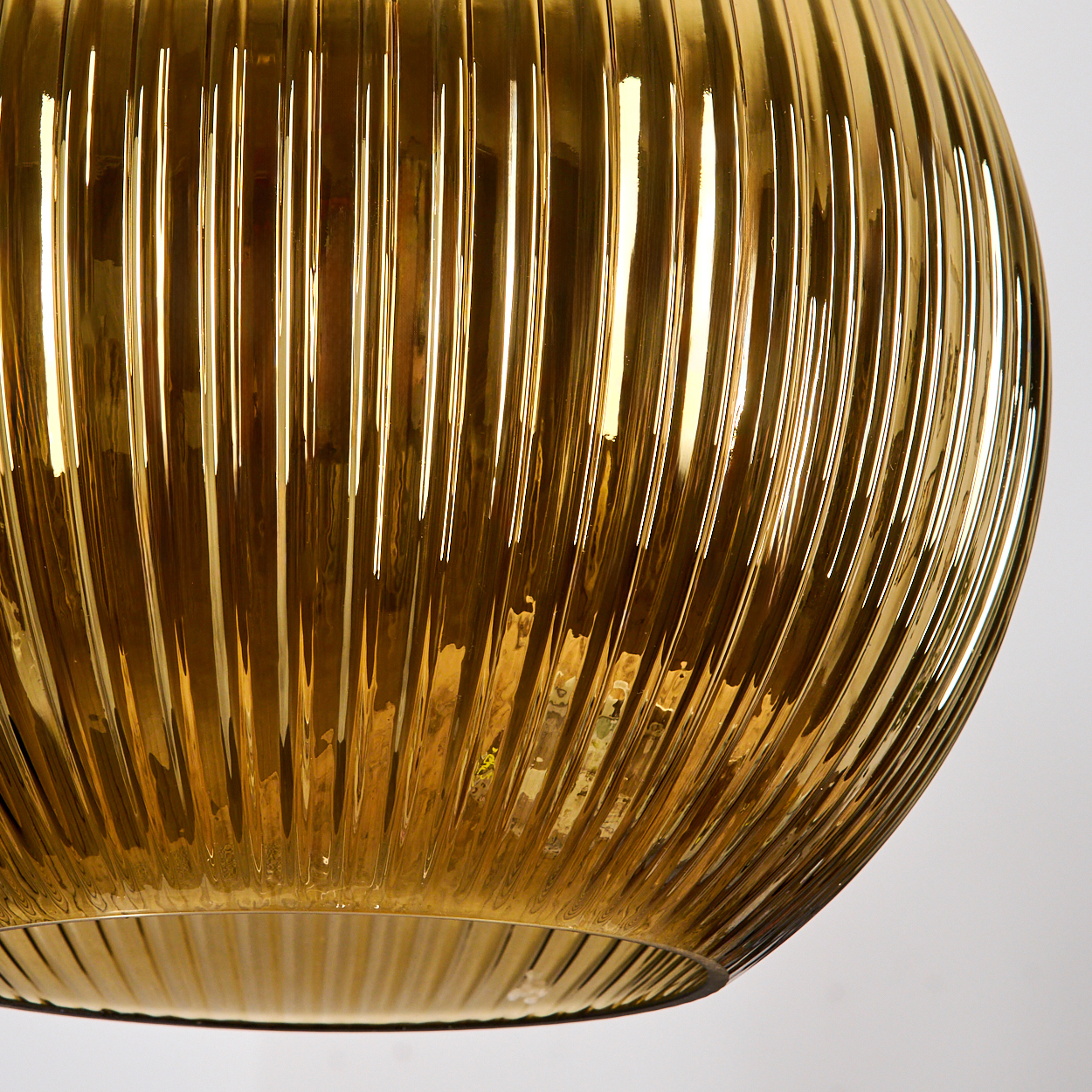 Nahaufnahme eines goldenen Glaslampenschirms. Vertikale Rippen bedecken die Oberfläche. Der Hintergrund ist weiß.