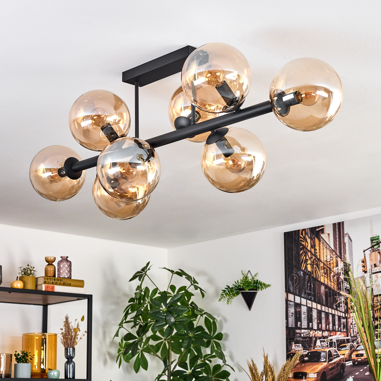 Moderne Deckenlampe mit mehreren bernsteinfarbenen Glaskugeln. Schwarzer Rahmen. Pflanzen, Regale mit Dekoration und ein Stadtbild im Hintergrund.