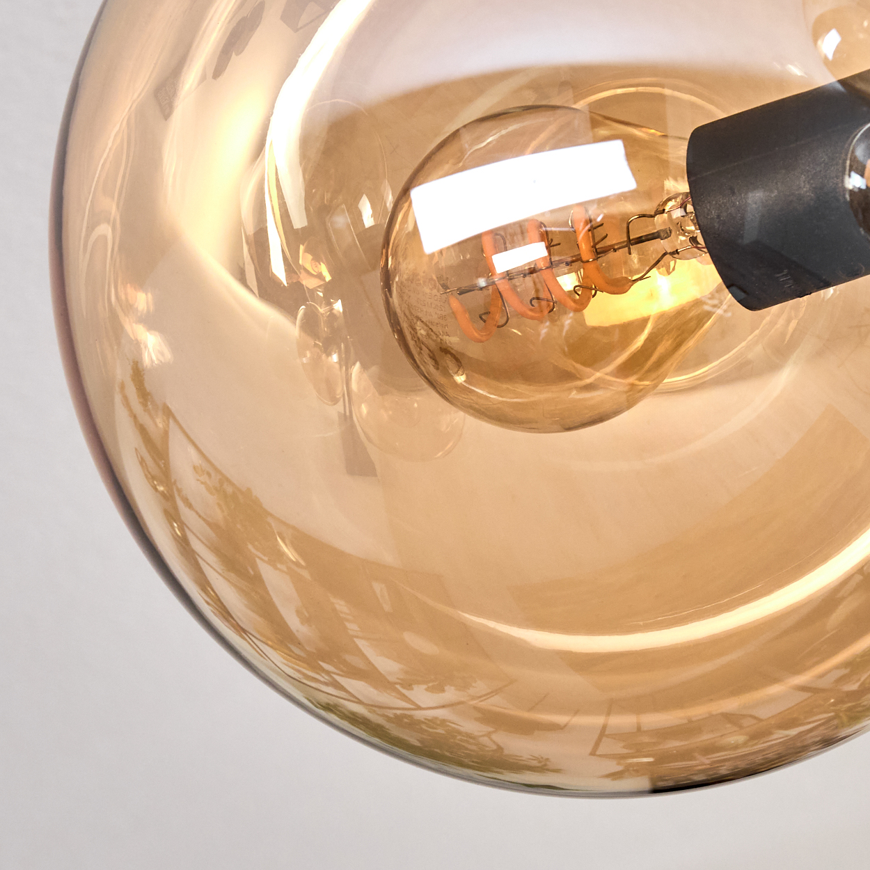 Nahaufnahme einer Glühbirne in einer transparenten, bernsteinfarbenen Glaskugel. Die Glühbirne leuchtet und zeigt ihren Innenfaden.