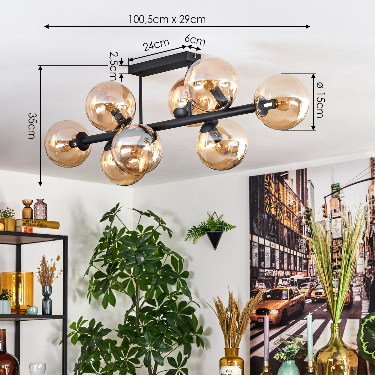 Eine moderne Deckenlampe mit goldfarbenen Glaskugeln. Ein schwarzer Metallrahmen trägt die Lichter. Pflanzen und ein Stadtbild sind im Hintergrund.