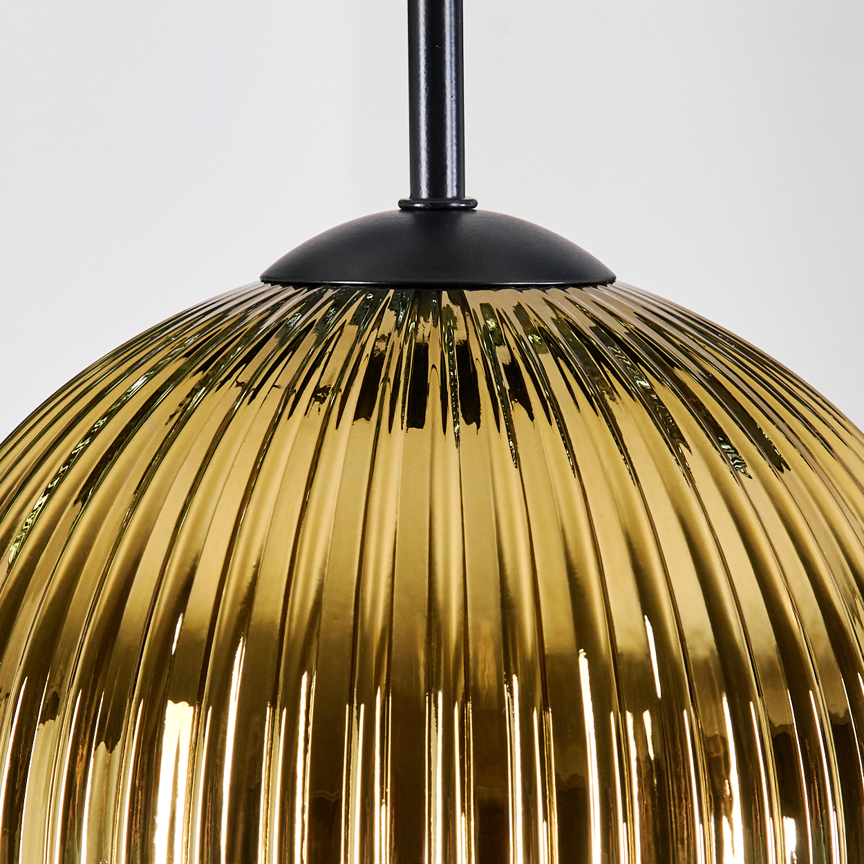 Nahaufnahme einer goldenen, gerippten Glas-Hängelampe. Schwarzer Metallschaft und Baldachin vor weißem Hintergrund.