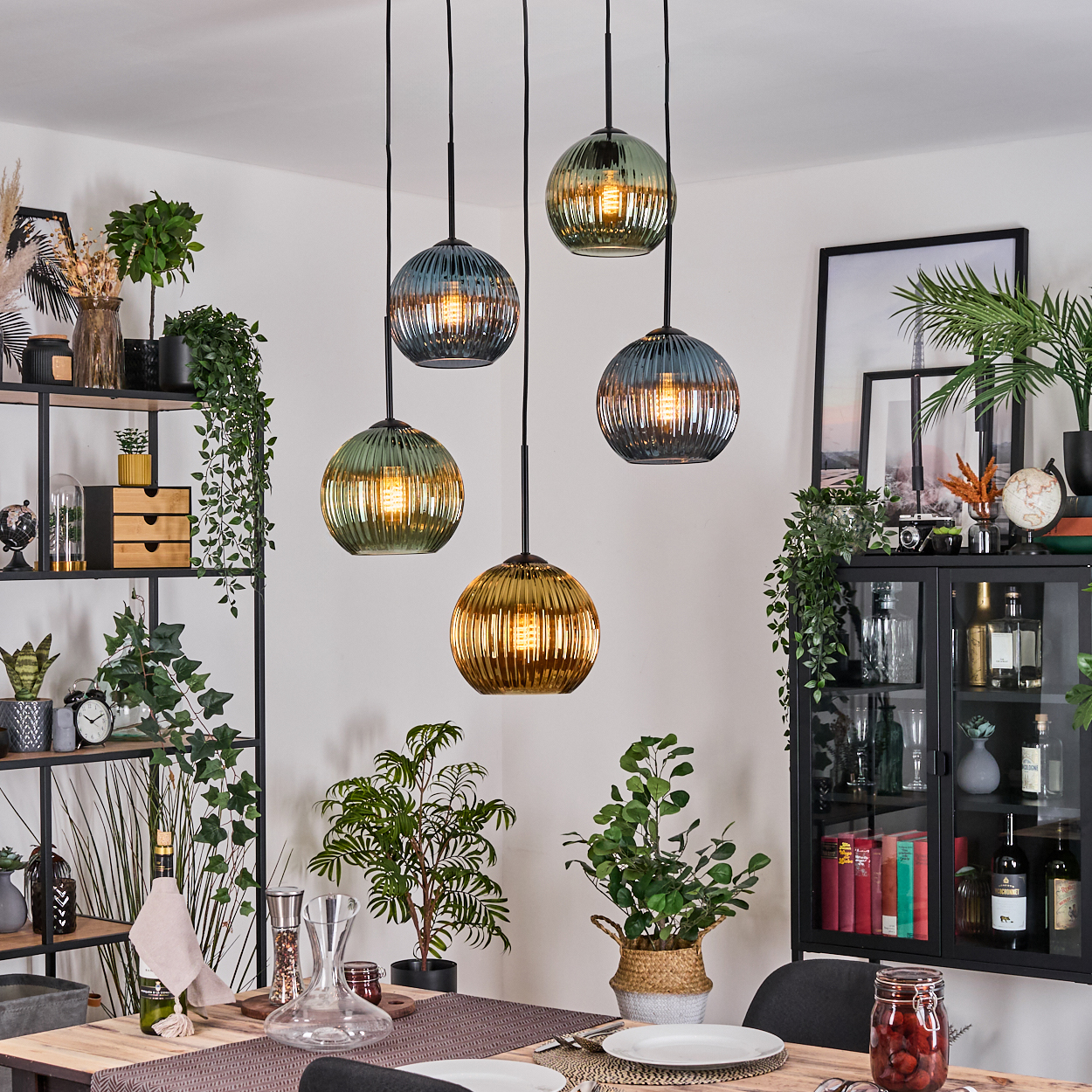 Esszimmer mit Hängelampen. Pflanzen und Möbel sind sichtbar. Die Lampen sind aus Glas und kugelförmig.