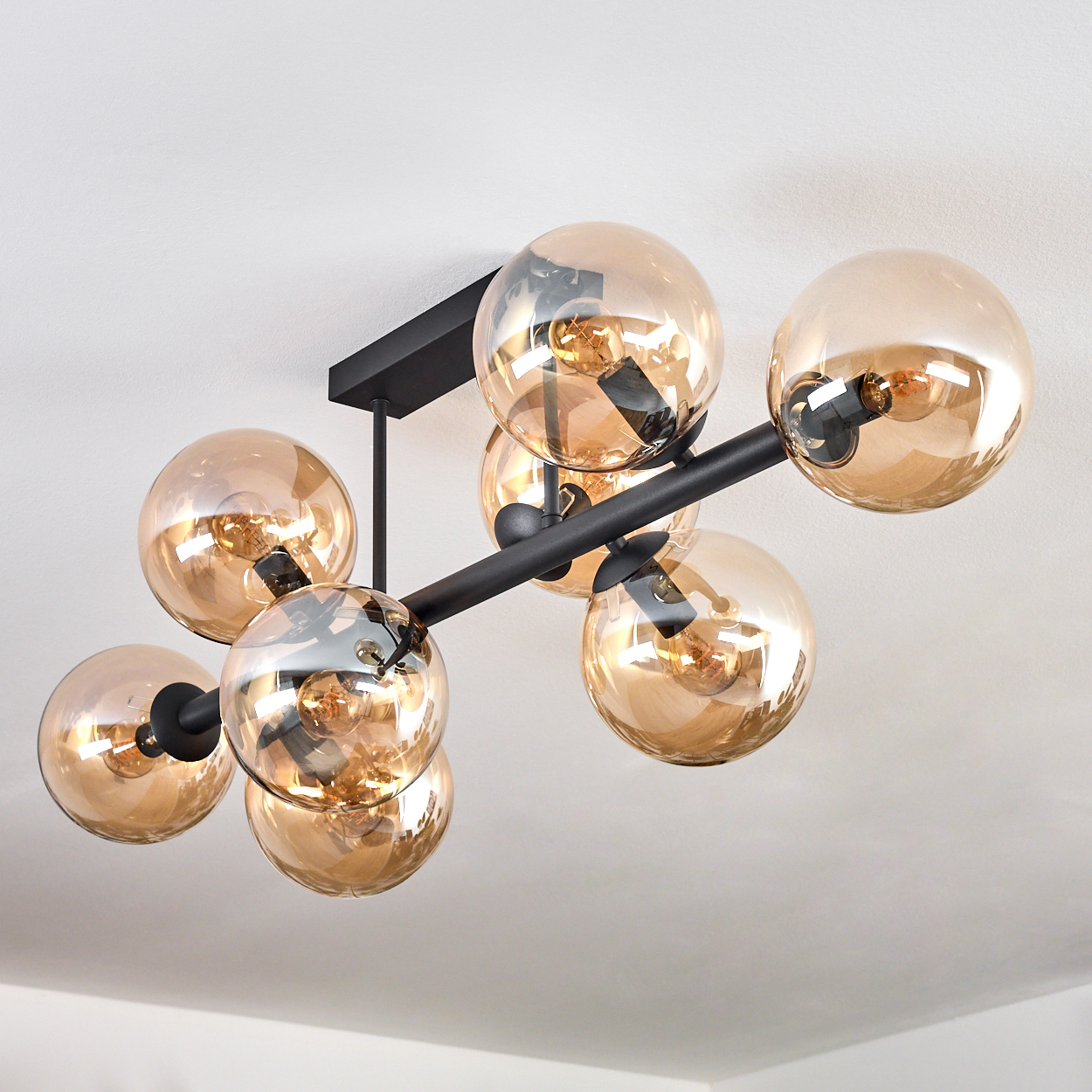 Moderne Deckenleuchte mit kugelförmigen, bernsteinfarbenen Glasschirmen und schwarzen Metallarmen. Glühbirnen im Inneren der Schirme sind sichtbar.