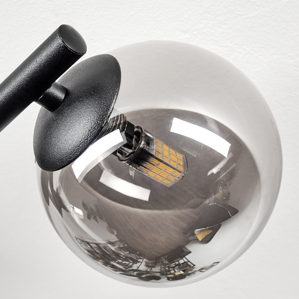 Nahaufnahme einer modernen Lampe. Sie hat einen schwarzen Arm, einen runden schwarzen Schirm und eine transparente Glaskugel mit einer LED-Leuchte.