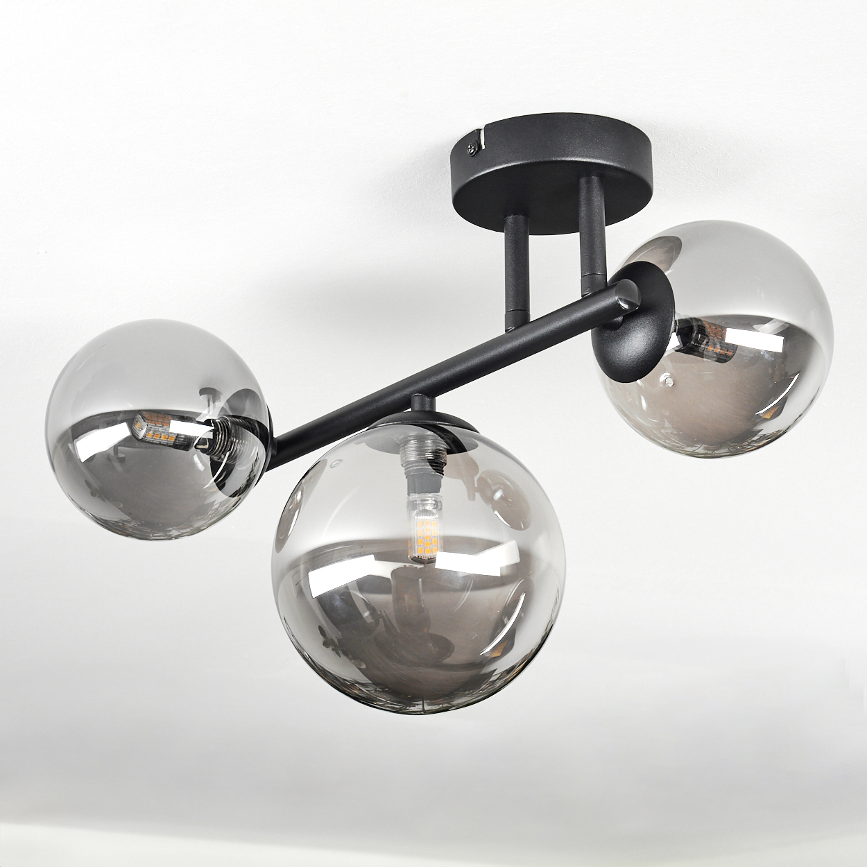 Eine moderne Deckenleuchte mit drei rauchfarbenen Glaskugeln. Schwarze Metallarme und -befestigung an einer weißen Decke.