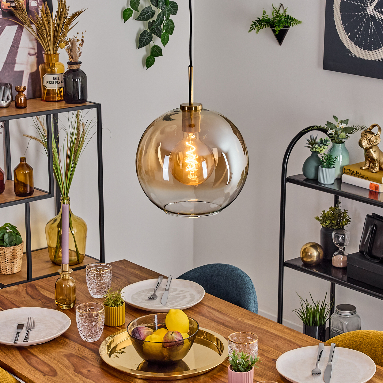 Ein Esstisch mit goldenem Kronleuchter, gedeckt mit Tellern, Gläsern und einer Obstschale. Regale mit Dekoration im Hintergrund.