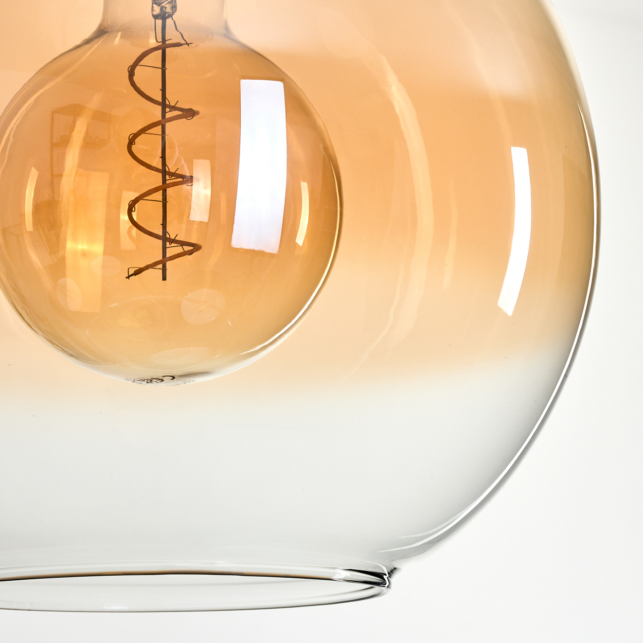 Nahaufnahme einer Glasleuchte. Das äußere Glas ist unten klar und oben orange. Im Inneren befindet sich eine runde Glühbirne.
