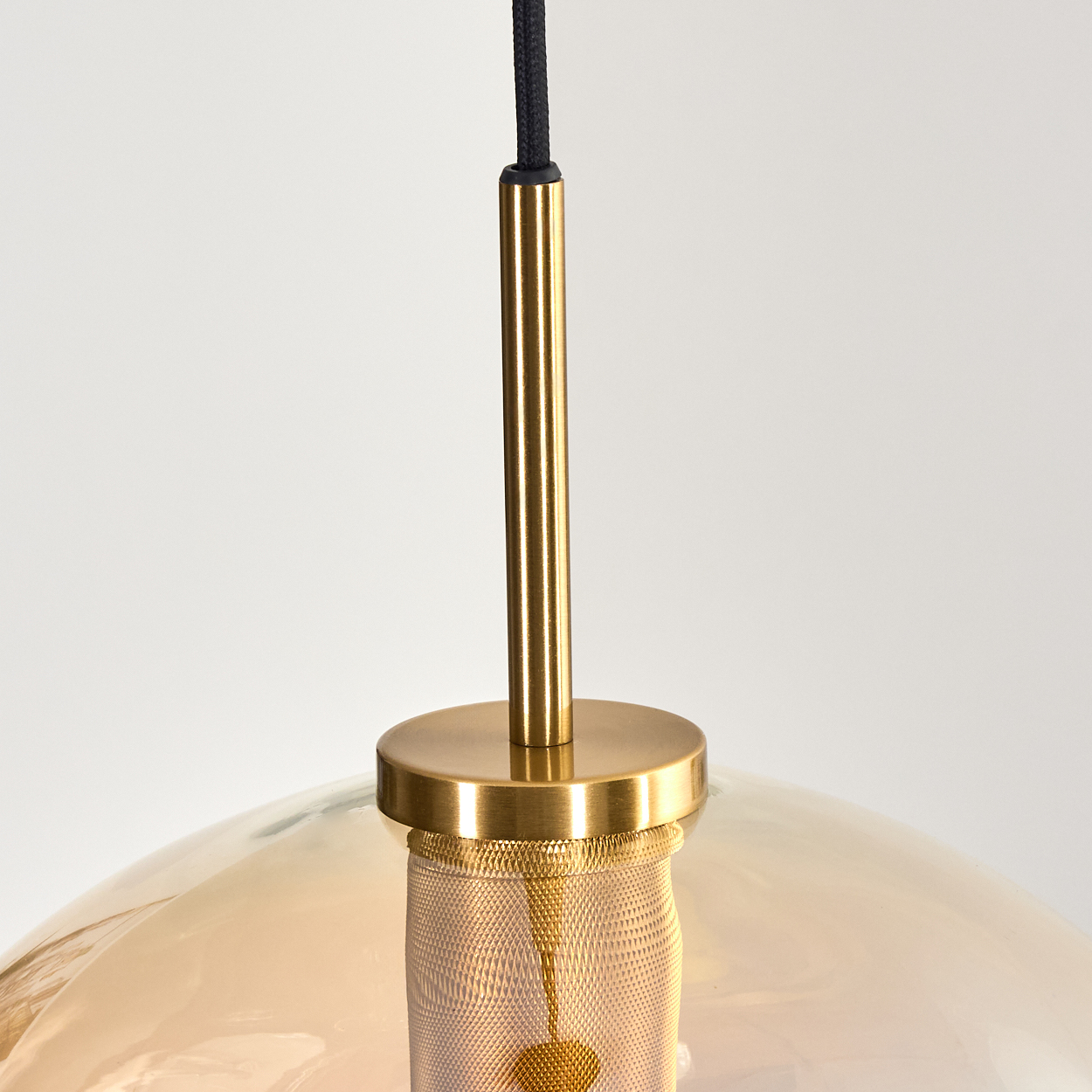 Nahaufnahme einer modernen Pendelleuchte. Sie hat einen goldfarbenen Metallrahmen, einen beigefarbenen Glasschirm und ein schwarzes Netzkabel.