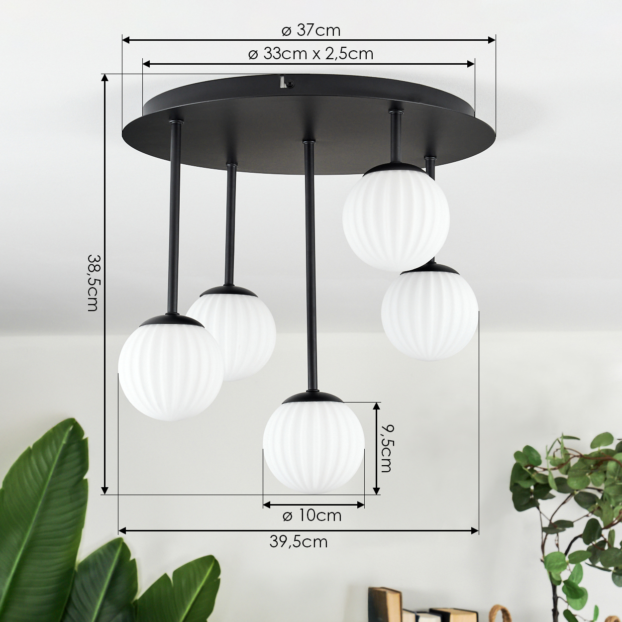 Moderne schwarze Deckenlampe mit fünf weißen Kugelleuchten. Maße sind angegeben. Grüne Pflanzen im Vorder- und Hintergrund.