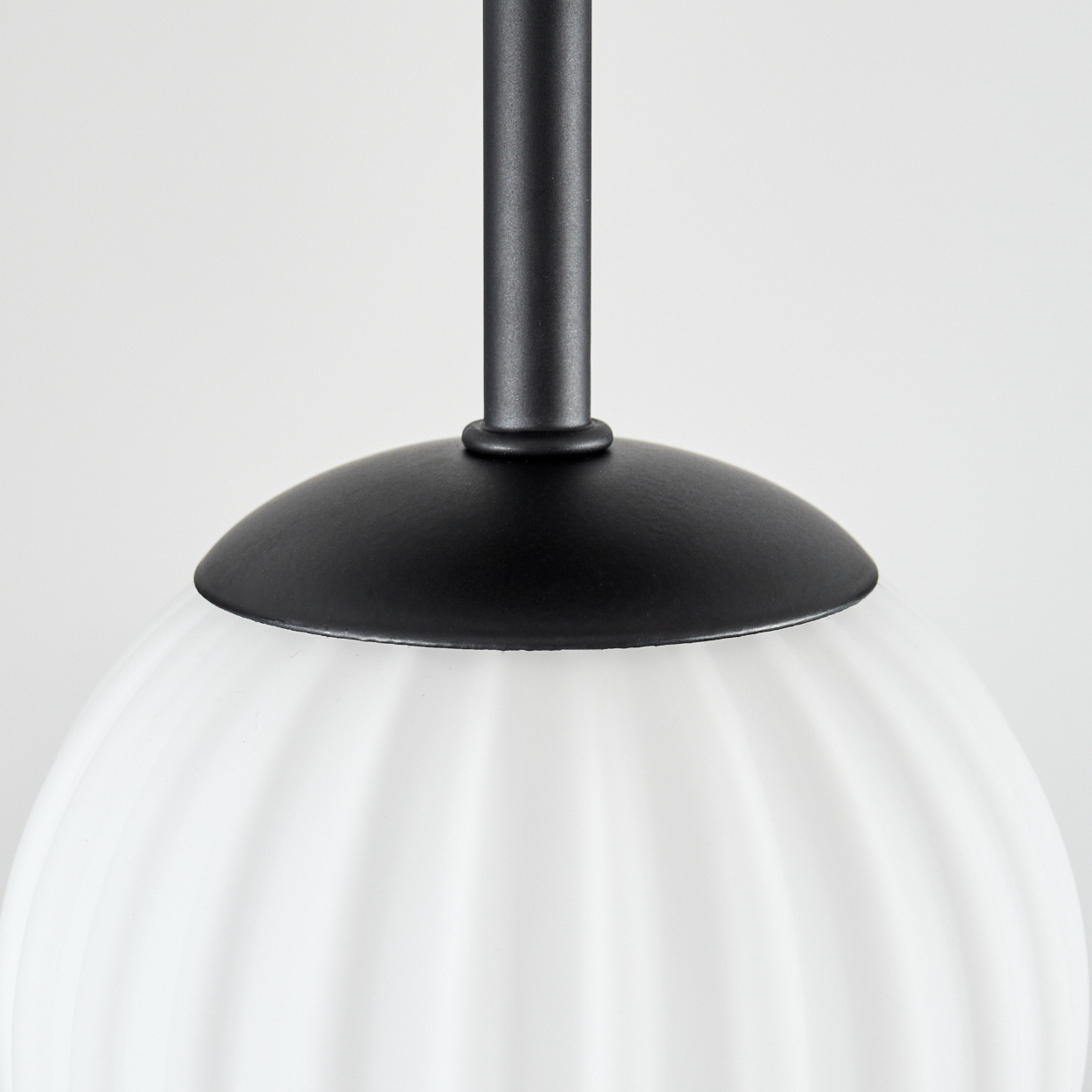 Nahaufnahme einer Lampe. Schwarzer Metallschaft und -schirm über einem weißen, gerippten Glaskolben. Einfarbiger weißer Hintergrund.