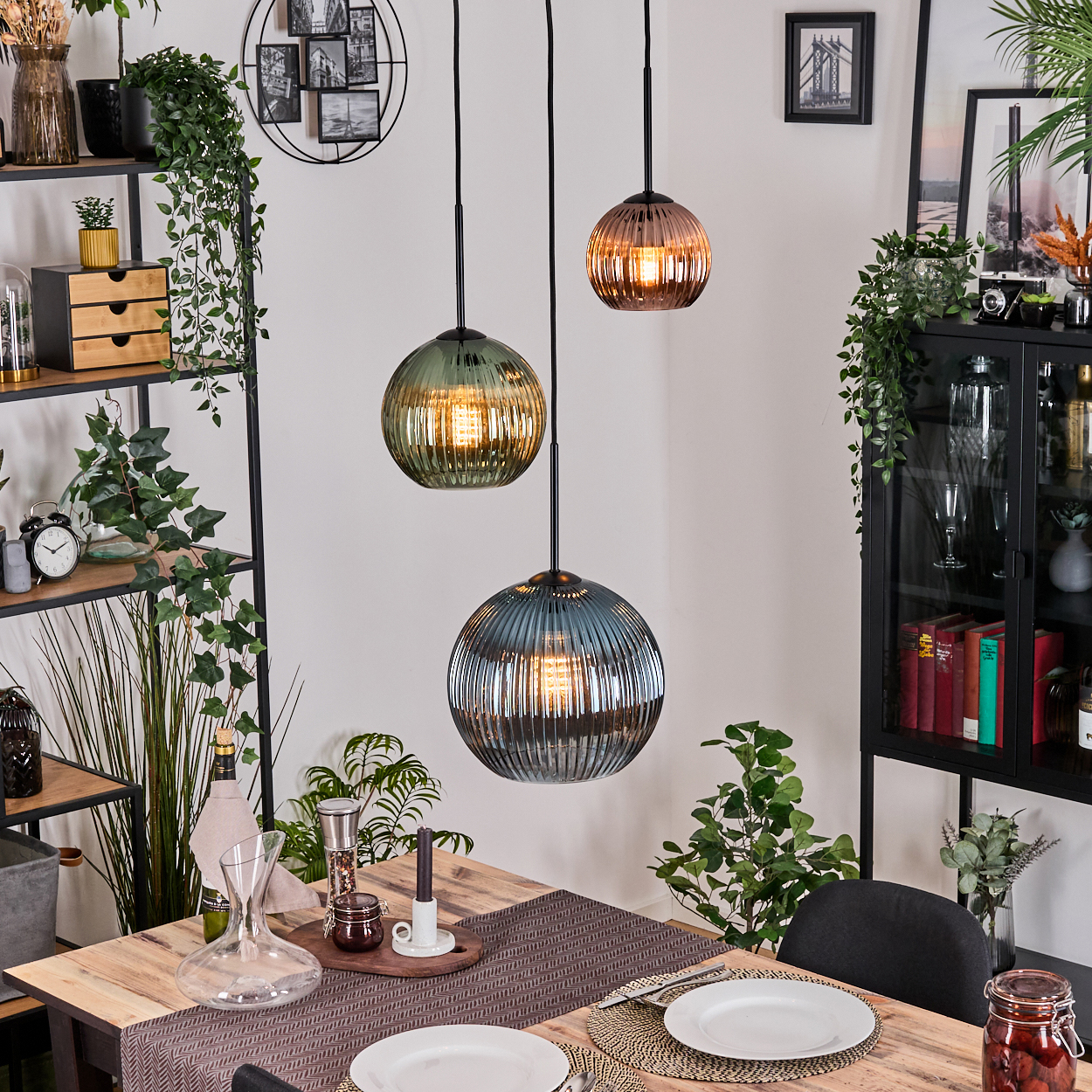 Esszimmer mit drei Hängelampen. Holztisch gedeckt. Regale mit Pflanzen und Dekor sind sichtbar.