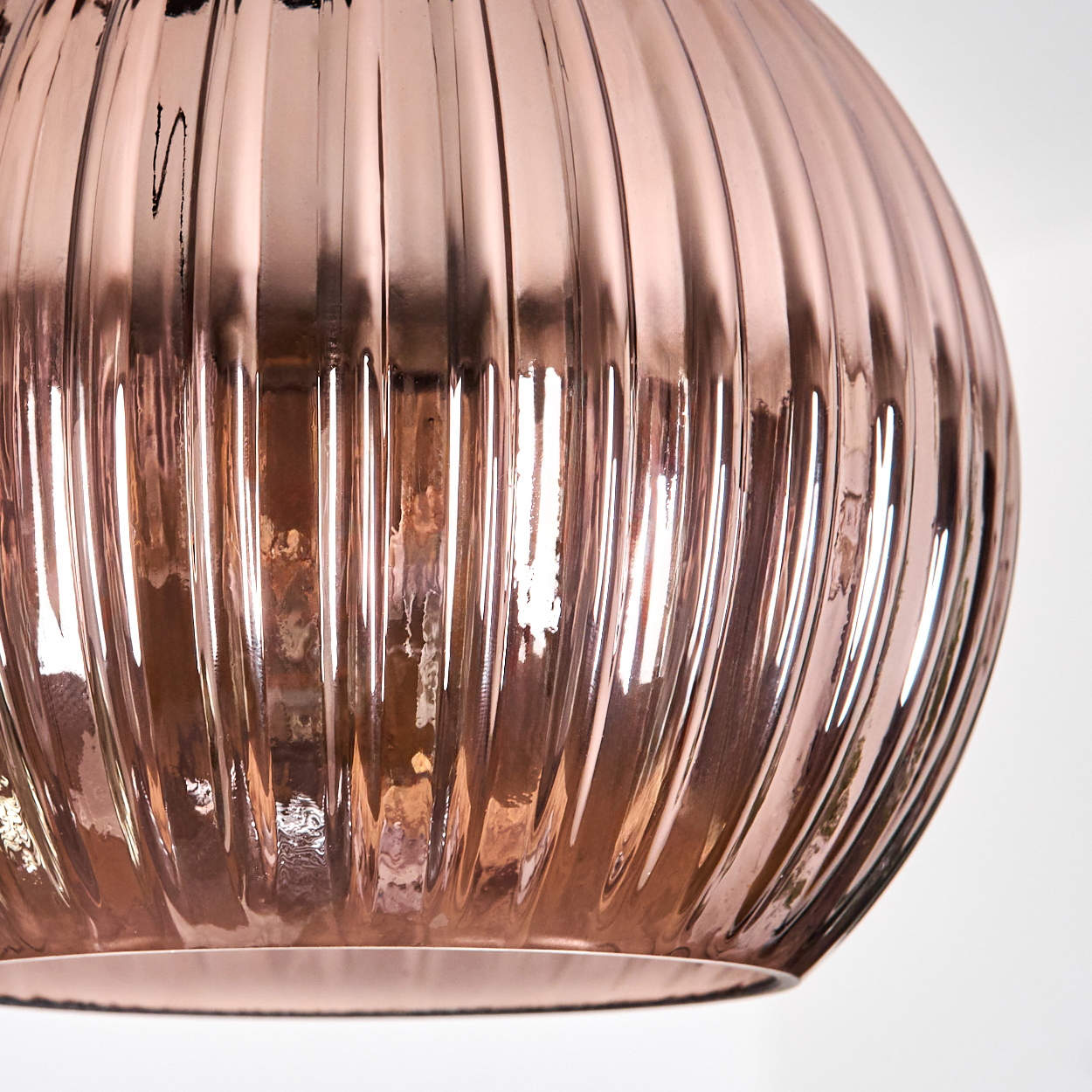 Nahaufnahme eines roségoldenen Glasobjekts mit vertikalen Rippen. Der Hintergrund ist weiß. Licht reflektiert sich auf der Oberfläche.
