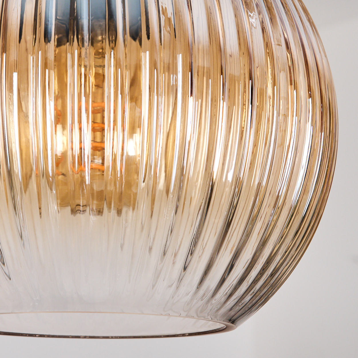 Nahaufnahme einer dekorativen Glaslampe. Die Lampe hat eine warme Bernsteinfarbe mit vertikalen Rippendetails. Der Hintergrund ist eine schlichte weiße Wand.