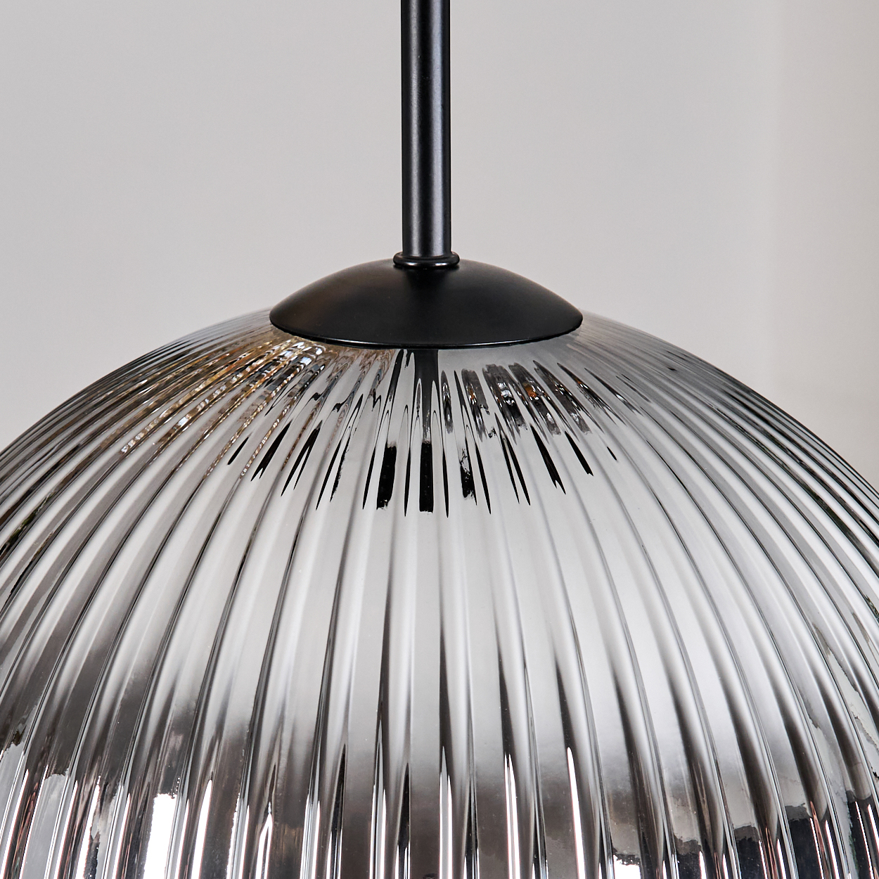 Nahaufnahme eines Lampenschirms aus Glas mit vertikalen Rippen. Er ist an einer schwarzen Metallstange und -kappe aufgehängt, vor weißem Hintergrund.