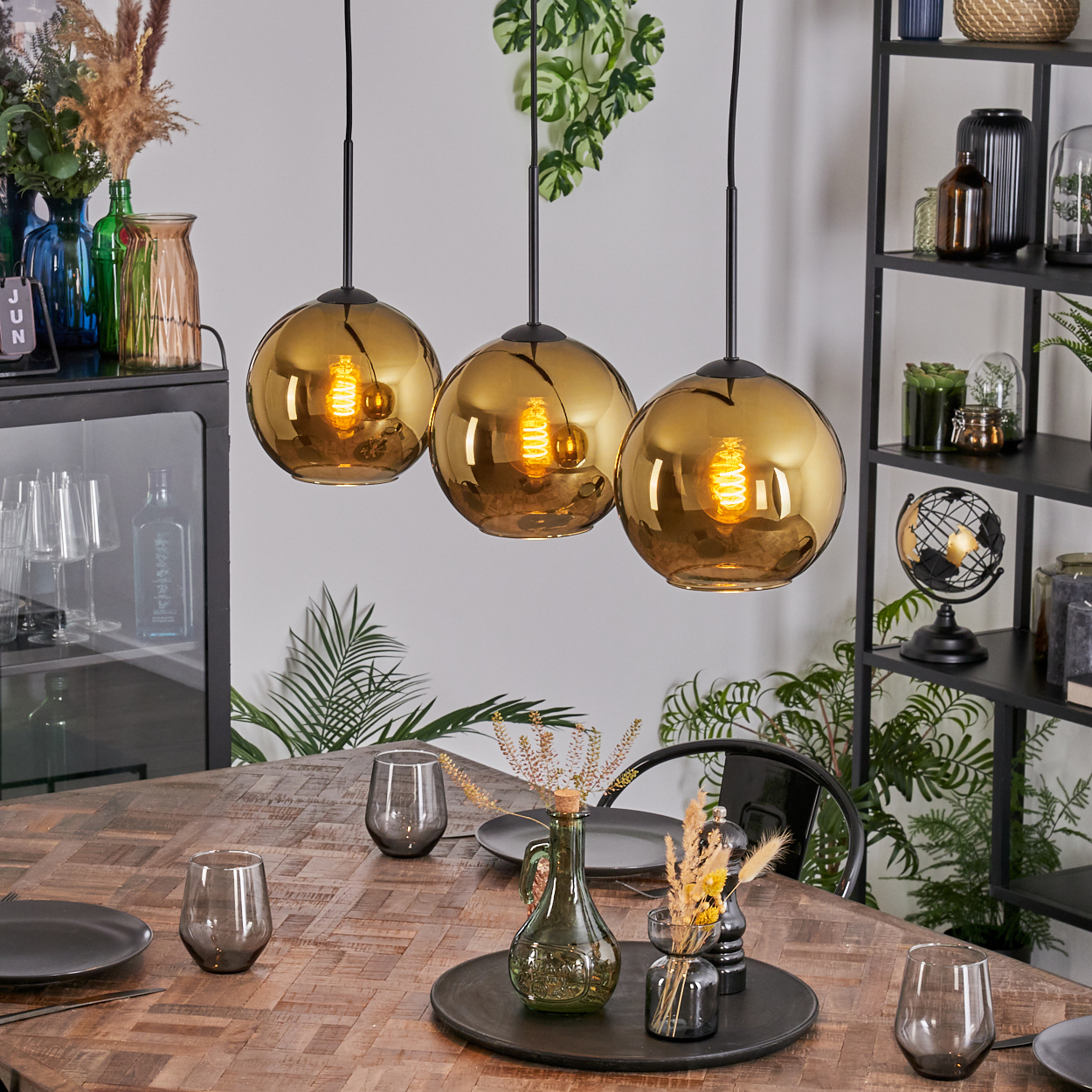 Esszimmer mit Holztisch, drei Hängelampen und verschiedenen Dekorationsartikeln auf einem Regal und dem Tisch.