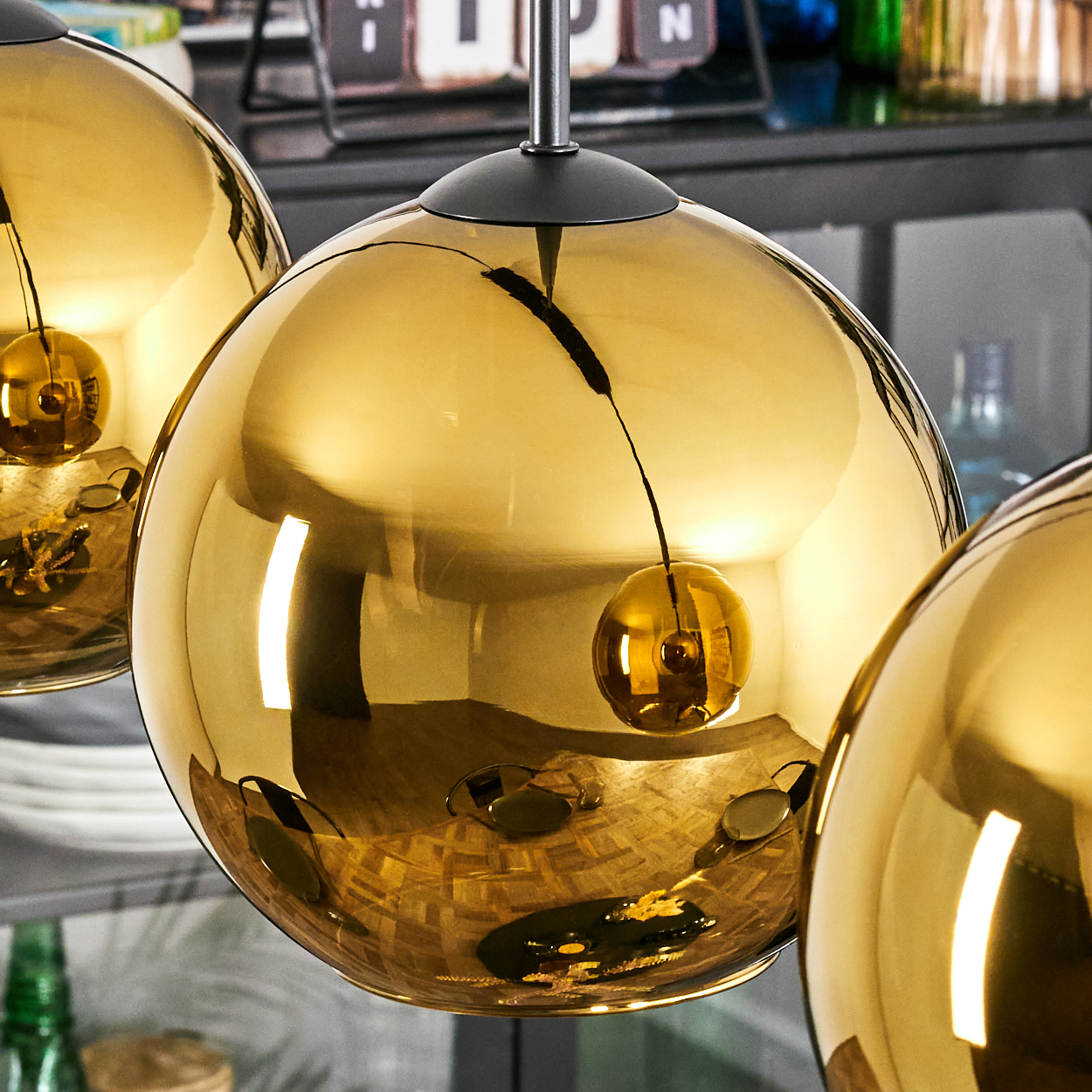 Nahaufnahme von drei goldenen, kugelförmigen Pendelleuchten. Reflektierende Oberflächen mit sichtbaren Schatten und Reflexionen. Hintergrund unscharf.